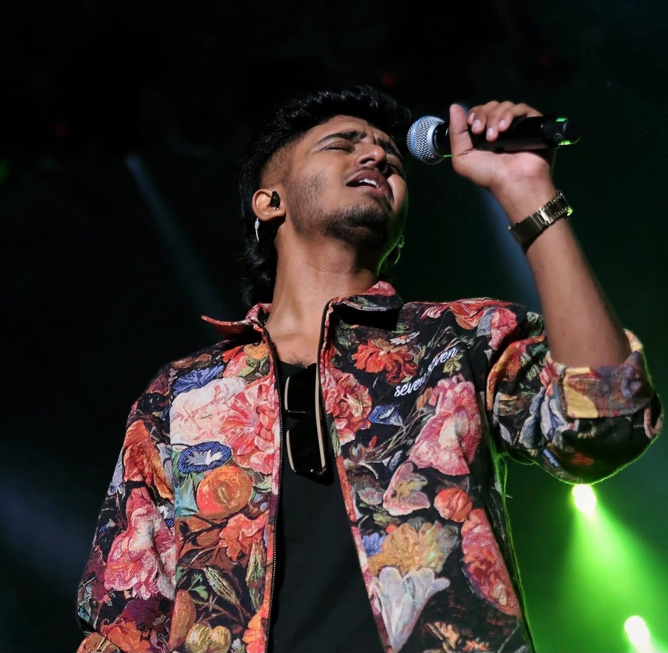 Sai Abhyankkar singing under green stage light at his live concert