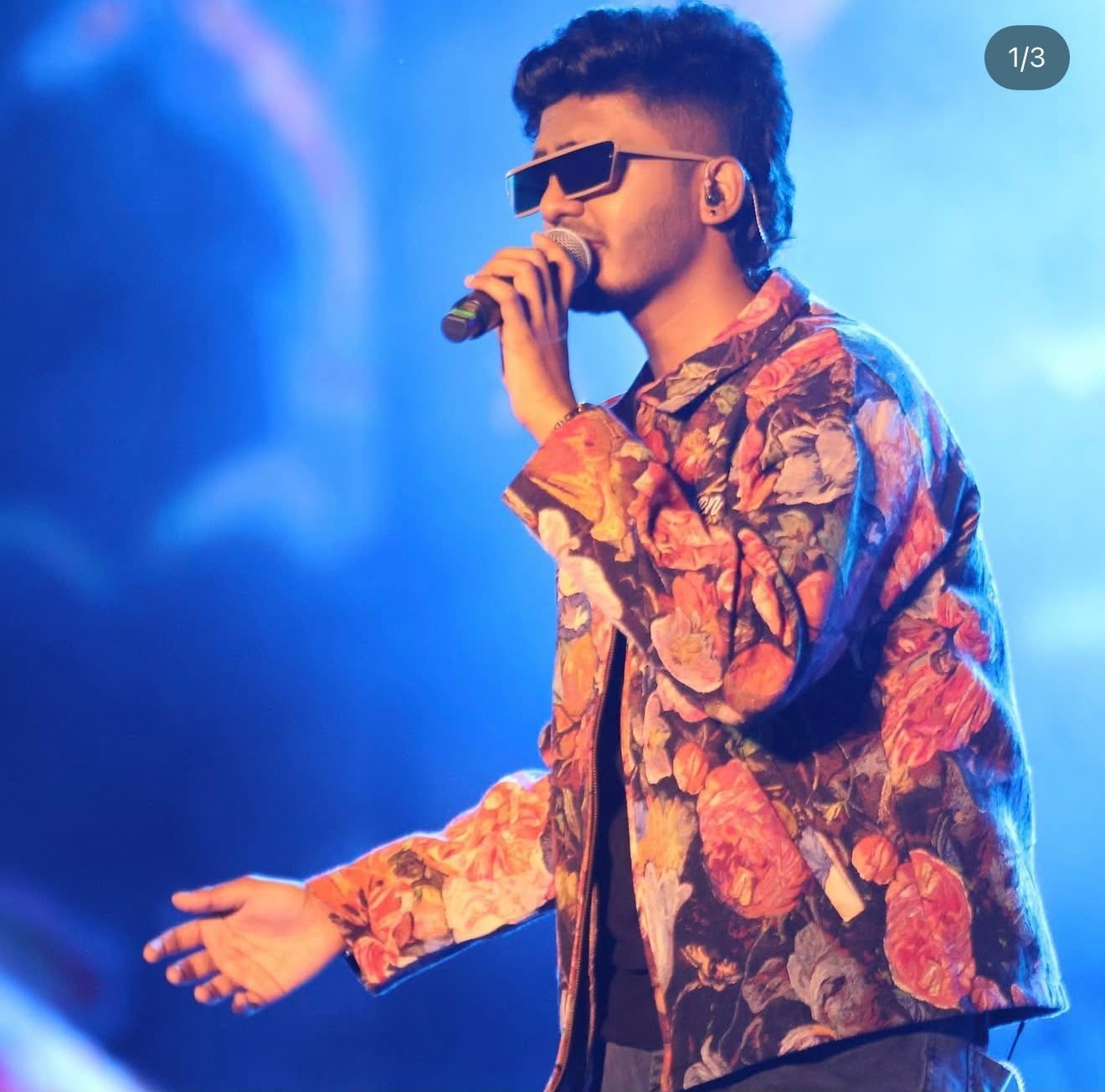 Sai Abhyankkar performing with microphone in hand under blue concert lighting